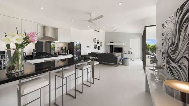 A modern kitchen with a central island, bar stools, and a dining area with a sofa.