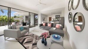 A modern living room with a grey sofa, a coffee table with a vase of flowers, and a dining area with a table and chairs.