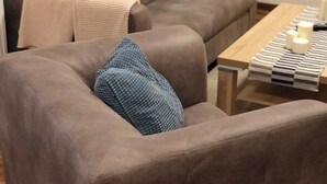 Un soggiorno con un divano marrone, un cuscino blu, un tavolino in legno con candele e una lampada sullo sfondo.