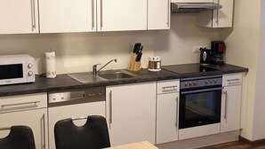 Una cucina compatta con mobili bianchi, un forno a microonde, una macchina da caffè e un'lavastoviglie.