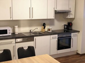 Una cocina compacta con armarios blancos, microondas, cafetera y lavavajillas.