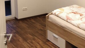 Una camera da letto con un letto in legno, un piccolo cassetto bianco e una porta che dà su un balcone.