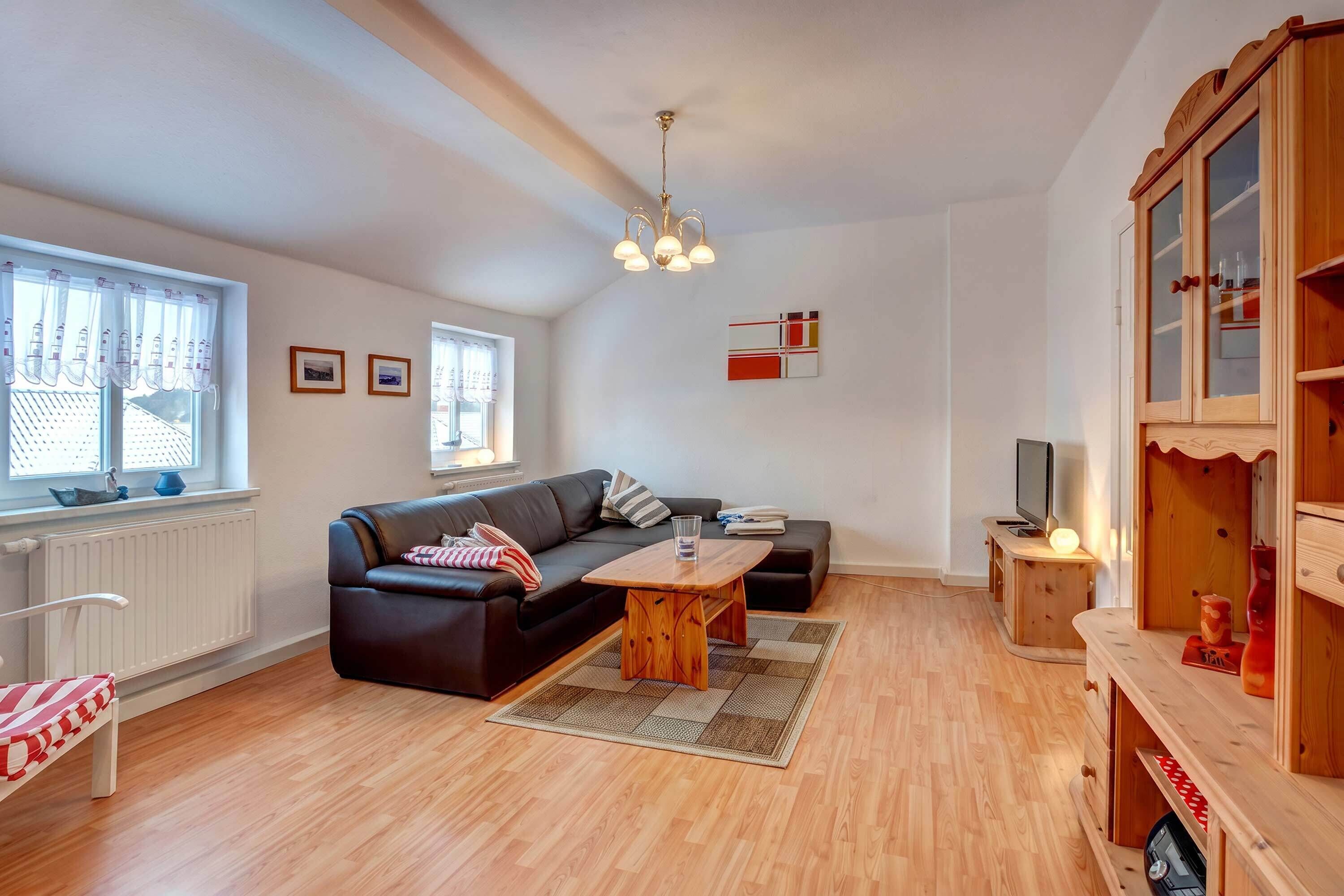A modern living room with a black leather sofa, a wooden coffee table, and a television on a wooden stand.