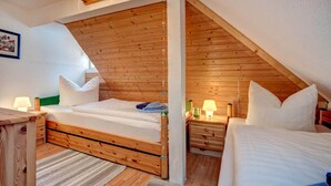 Un dormitorio acogedor en el ático, con vigas de madera, dos camas, mesitas de noche y una lámpara colgante.