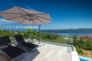 Enjoy a serene lakeside view from this outdoor terrace, surrounded by lush greenery and overlooking the distant mountains.