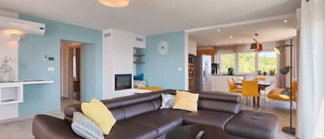 A modern living room with a sectional sofa, a coffee table, and a dining area with yellow chairs.