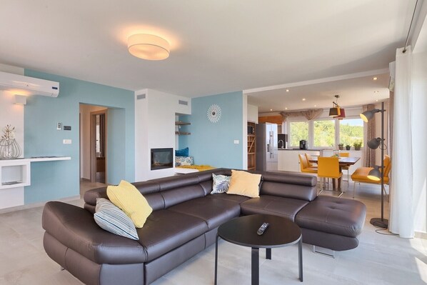A modern living room with a sectional sofa, a coffee table, and a dining area with yellow chairs.