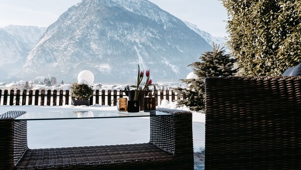 A glass-top table with wicker chairs, a wooden fence, and a snow-covered mountain in the background.