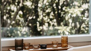 A window with a view of trees and a shelf with various glassware.