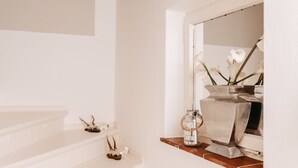 A bathroom with a white sink, a mirror, and decorative items including a vase with flowers and a metal container.