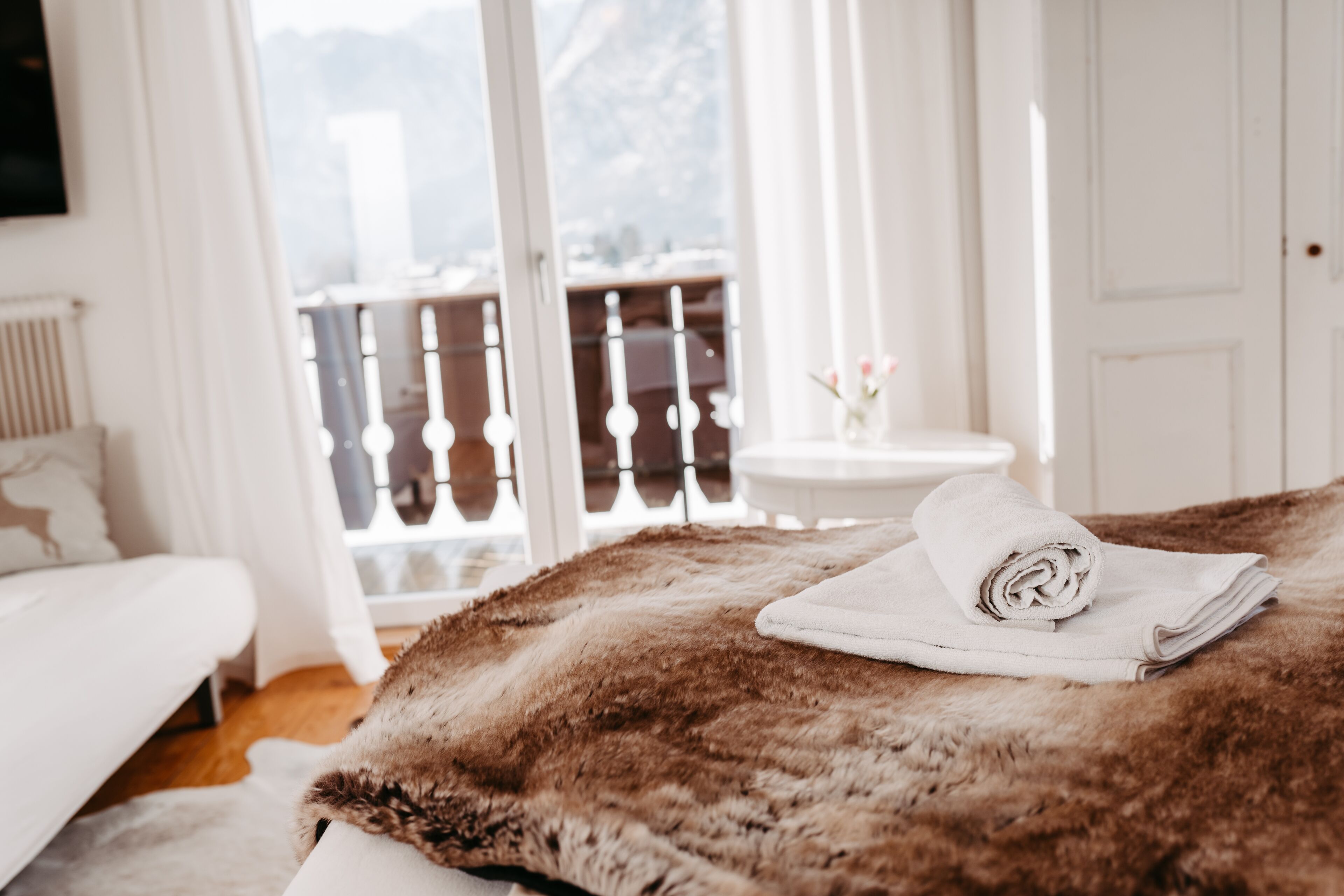 Een slaapkamer met een groot raam, een bed met een bruine, pluizige deken en een witte handdoek op het bed.