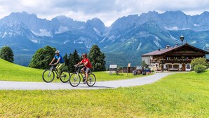 A mountain bike path with two cyclists, a wooden building with a balcony, and a mountain backdrop. - Wittner's B&B - small, fine and warm (S öll)