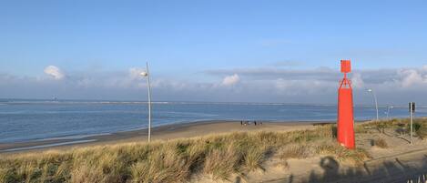 Une plage avec une bouée rouge bien visible, des dunes herbeuses et une vue dégagée sur la mer.