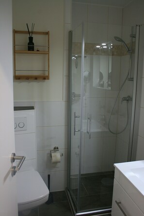 A bathroom with a toilet, a glass shower enclosure, and a white sink. - Apartment "Beachfront with sea view and sunny balcony" (Borkum)