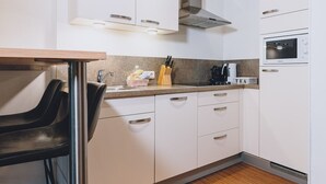 A compact kitchen with white cabinets, a stainless steel sink, a microwave, and a coffee maker. - Alpine City Living - TOP 32, City center & balcony (Zell am See)