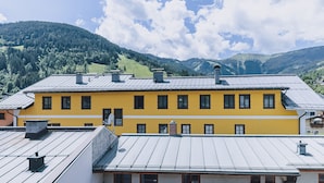 A yellow building with multiple windows and a metal roof, surrounded by green hills and a partly cloudy sky. - Alpine City Living - TOP 32, City center & balcony (Zell am See)