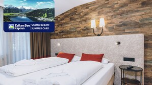 A hotel room with a large bed, two pillows, a nightstand, and a wall-mounted lamp. - Alpine City Living - TOP 32, City center & balcony (Zell am See)
