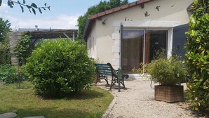 Ein Haus mit einem Schotterweg, einem grünen Rasen und einer Terrasse mit einer Bank und einem Tisch.