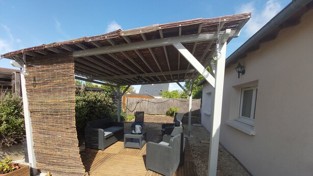 Eine überdachte Terrasse mit Gartenmöbeln, einer Pergola und einem Kiesboden.
