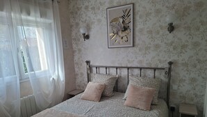 Ein ordentlich bezogenes Bett mit gemustertem Bettbezug und Kissen, eine Wandleuchte sowie blumengemusterte Tapete.