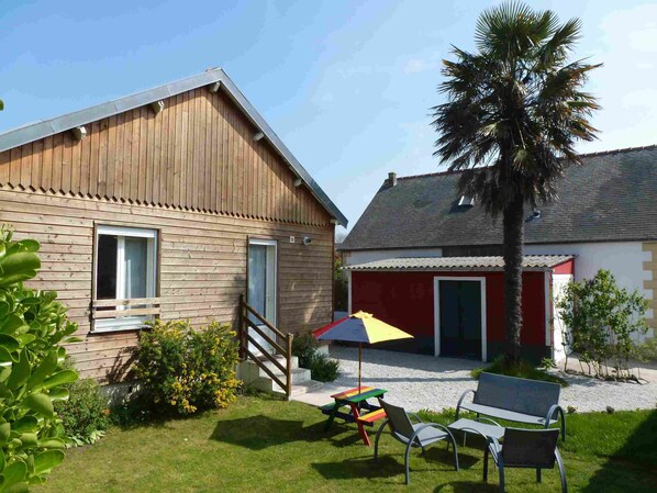 A wooden house with a red door and a covered patio area with a table and chairs. - In Dinard, house with garden close to the sea - Gîte "Aod Gwer-Vein (Dinard)