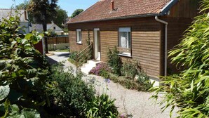 A wooden house with a tiled roof, a small porch, and a garden with various plants and flowers. - In Dinard, house with garden close to the sea - Gîte "Aod Gwer-Vein (Dinard)