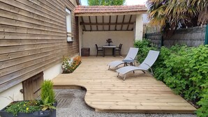 A wooden deck with two lounge chairs and a table, surrounded by greenery and a small garden area. - In Dinard, house with garden close to the sea - Gîte "Aod Gwer-Vein (Dinard)