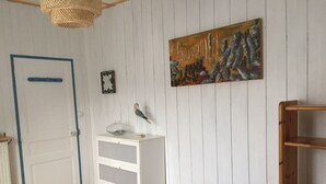 A room with a white door, a white dresser with drawers, a wooden shelf, a painting on the wall, and a hanging light fixture. - In Dinard, house with garden close to the sea - Gîte "Aod Gwer-Vein (Dinard)