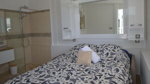 Habitación de hotel con cama, baño con ducha, espejo y toalla sobre la cama.