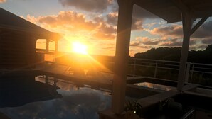 Un área de piscina con vista al atardecer, sillas de descanso y una zona de estar cubierta.