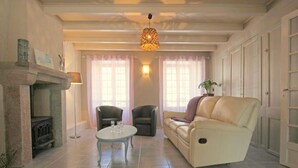 Un salon avec une cheminée, deux fauteuils, un canapé et un luminaire suspendu.