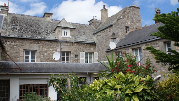 Un bâtiment en pierre avec un toit en pente, de nombreuses fenêtres et des antennes paraboliques.