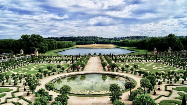 Ein formeller Garten mit einem zentralen Teich, symmetrischen Wegen und gepflegten Rasenflächen.