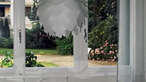 A room with a glass table, white chairs, and a view of a garden with pink flowers and greenery. - Fully furnished holiday apartment 4 * rated - very pleasant - 700 sq feet (Chambéry)