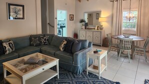 A living room with a sectional sofa, a glass coffee table, a white side table, a dining area with a round table and chairs, and a kitchen visible through an open door. - As seen on HGTV's Bahamas Life - Perfect Villa for an Island Getaway! (Paradise Island, Nassau)