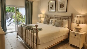 A bedroom with a bed, bedside tables, a ceiling fan, and a view of a patio with chairs and a wooden fence. - As seen on HGTV's Bahamas Life - Perfect Villa for an Island Getaway! (Paradise Island, Nassau)