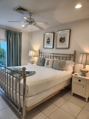 A bedroom with a bed, nightstands, a ceiling fan, and framed artwork on the wall.