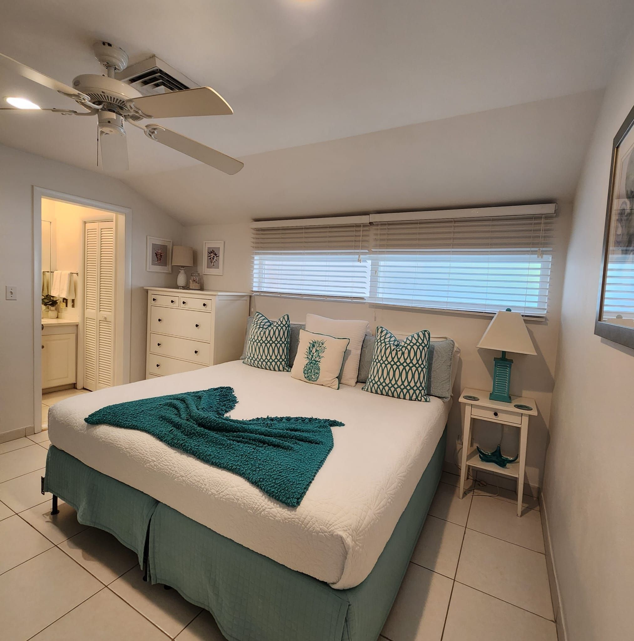 A bedroom with a bed, a ceiling fan, a window with blinds, a nightstand, and a lamp.