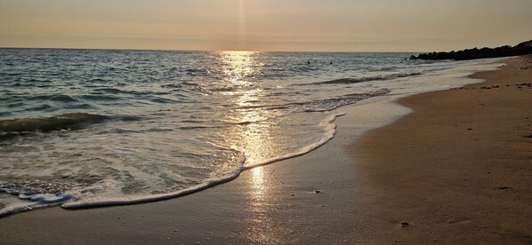 A beach with waves lapping onto the shore, a clear sky, and a calm sea.