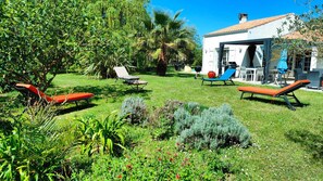 Ein Garten mit Sitzgelegenheiten im Freien, einem Grillplatz und einem weißen Gebäude mit einem Ziegeldach.
