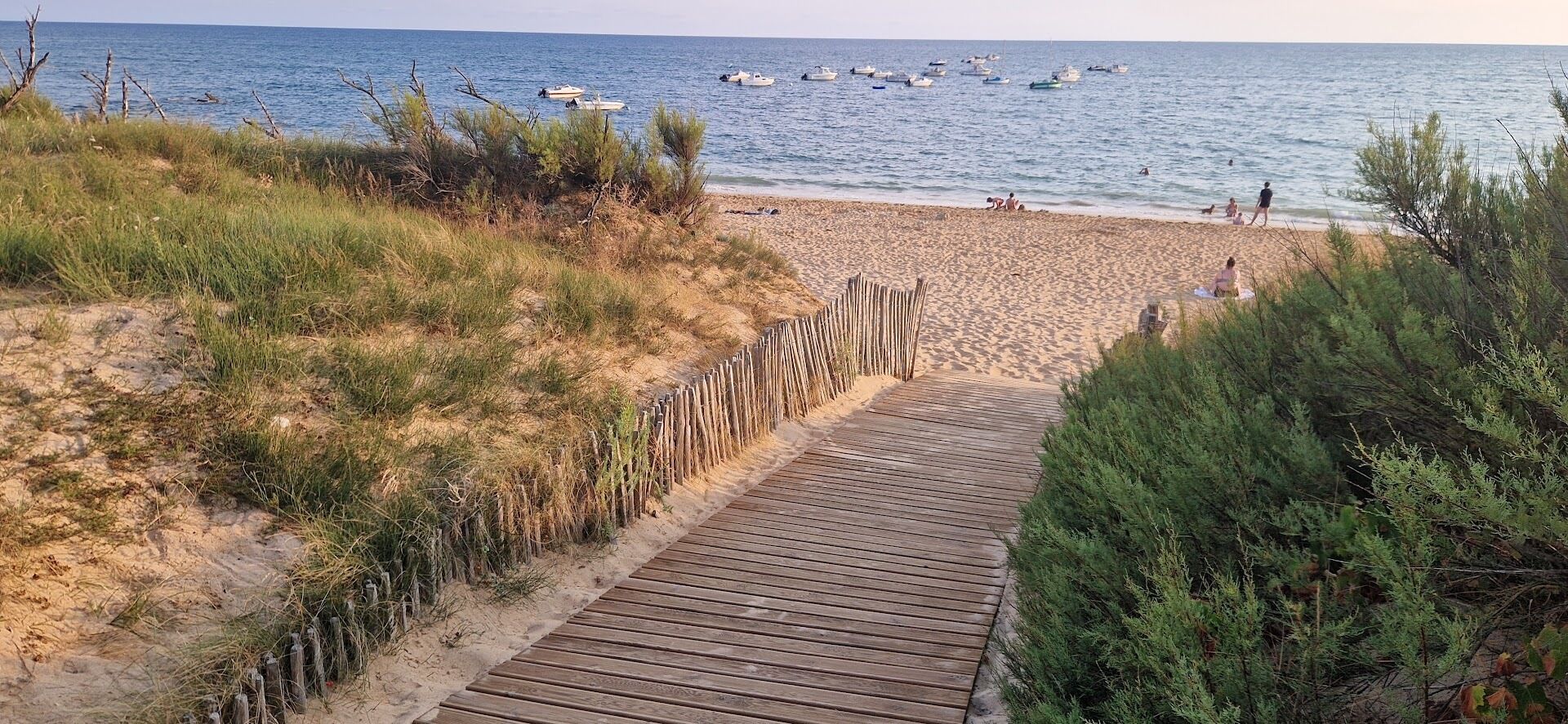 A wooden boardwalk leading to a sandy beach with boats in the water.