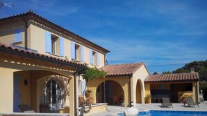 A two-story building with a swimming pool, outdoor seating, and a stone wall.