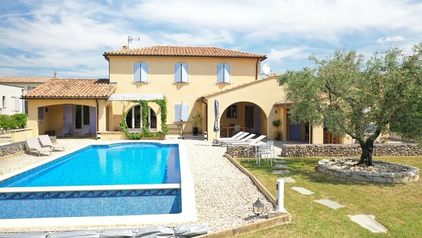 A villa with a swimming pool, outdoor seating, and a garden.