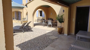 An outdoor patio with a table and chairs, a potted plant, and a door.