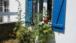 Een wit gebouw met blauwe luiken, een stenen muur en een raam met kantgordijnen.