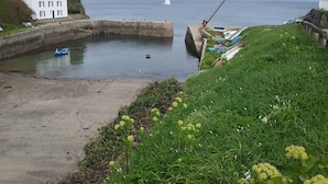Een kustgezicht met een wit gebouw, een klein bootje en een zeilboot in de verte.