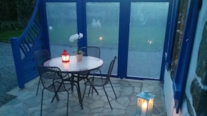 Een terras buiten met een ronde tafel en stoelen, een potplant en twee lantaarns.