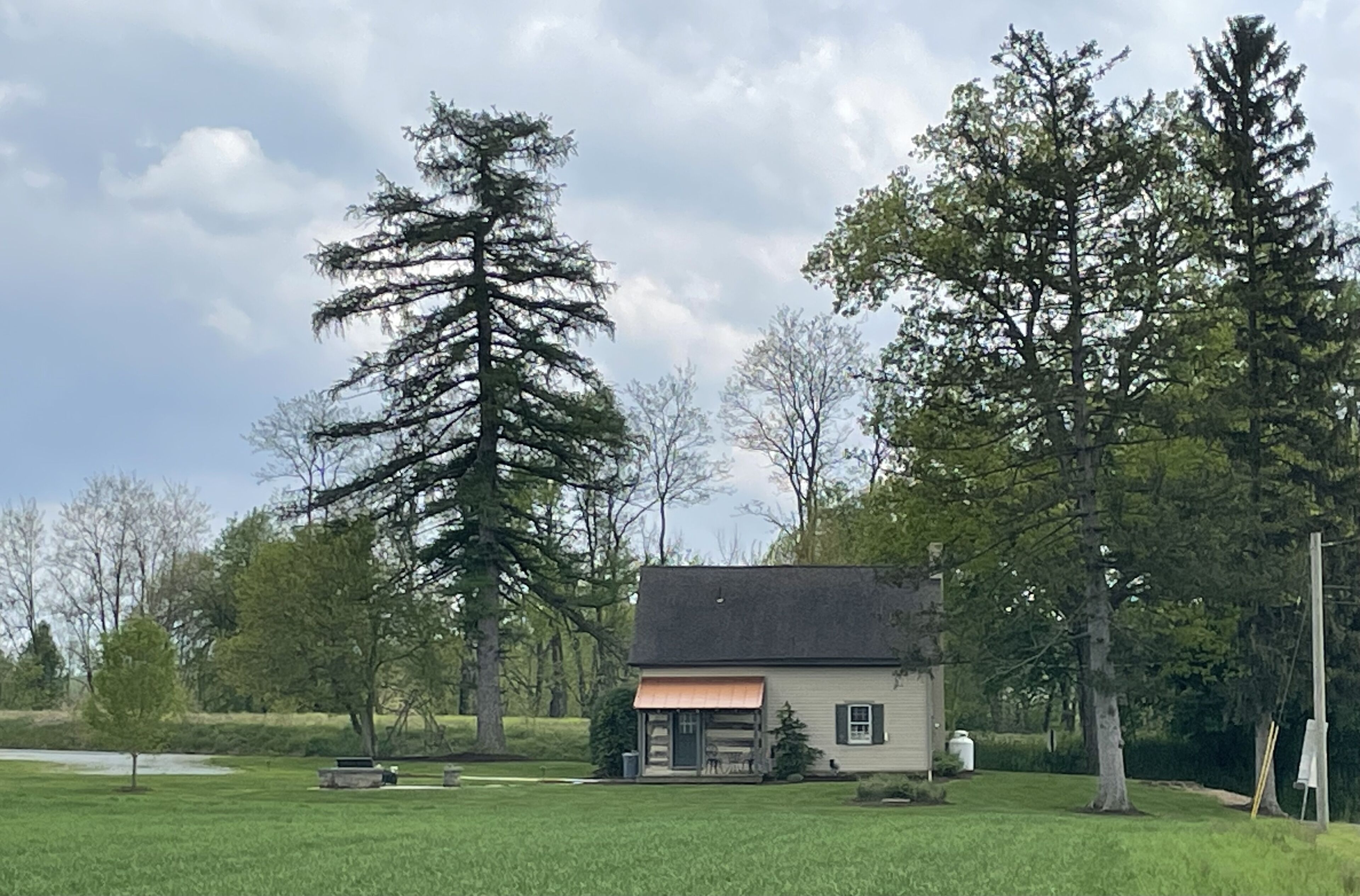 Une maison dotée d’un porche, entourée de grands arbres et bordée d’un champ verdoyant.