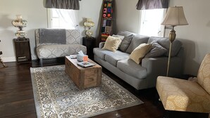Una sala de estar con un sofá gris, un sillón estampado, una mesa de centro de madera y una alfombra con diseño.