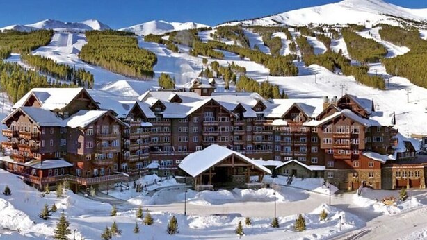 Ein großes Chalet mit mehreren Gebäuden, umgeben von schneebedeckten Bergen und Skipisten.